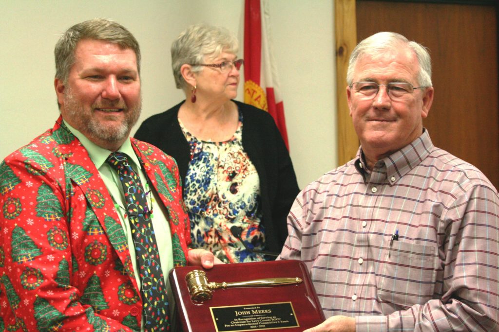 Outgoing Levy County Commission Chairman John Meeks receives a plaque from County Coordinator Wilbur Dean recognizing his five consecutive terms as chairman of the board. Commissioner Lilly Rooks can be seen in the background.