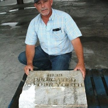 School Board member Brad Etheridge kneels behind a marble block engraved with the year 1939 and the words, "Dedicated To Our Youth." The time capsule is the rectangular copper box in front. The box is a bit weathered from the passage of 81 years.