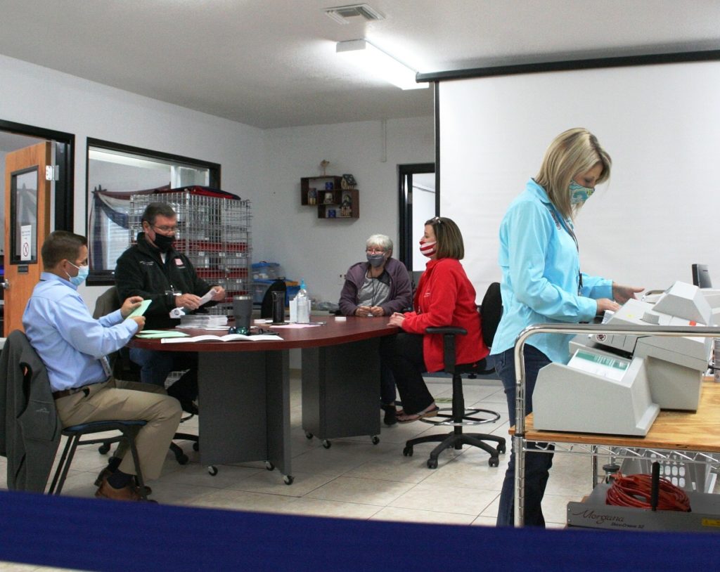 Assistant Elections Supervisor Jordan Lindsey opens absentee ballot envelopes on the right as canvassing board members - County Commission Chairman Matt Brooks, County Judge James T. Browning, County Commissioner Lilly Rooks (alternate member) and Elections Supervisor Tammy Jones open and review ballots.