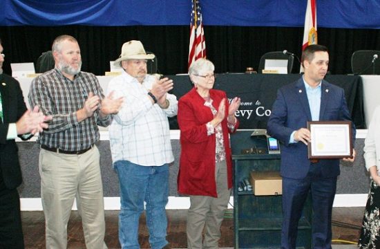 Levy County Commissioners John Meeks, Rock Meeks, Mike Joyner and Lilly Rooks applaud retiring Levy County Health Department Director Barbara Locke as Commission Chairman Matt Brooks presents her with a plaque recognizing 44 years of service to the county.