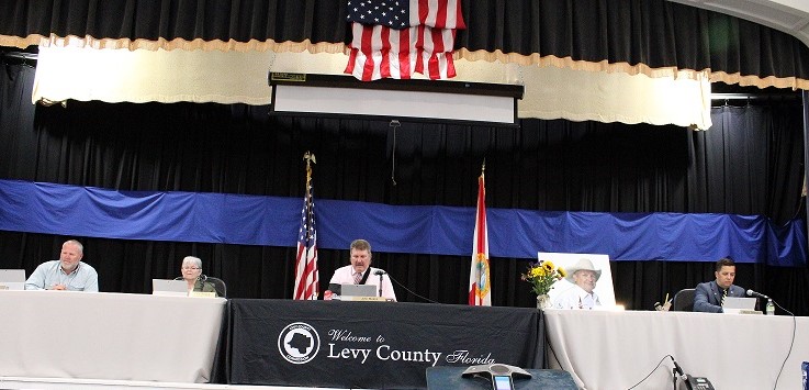 Levy County Commissioners offer a silent tribute to the late Commissioner Mike Joyner by erecting a poster-sized photo where he once sat at the dais.