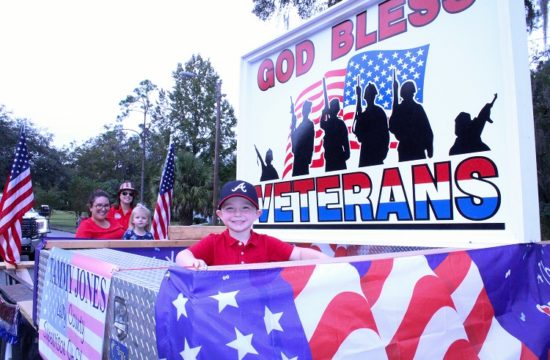 Tate Barber, grandson of Levy County Supervisor of Elections Tammy Jones, waves to bystanders as he rides on the front of her patriotic float in the Levy County Veterans Parade Thursday.