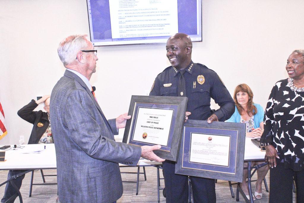 Mayor Jerry Robinson presents incoming Police Chief Mike Rolls with a plaque recognizing his new stature in the department and a second plaque honoring his service. His mother, Sandra Rolls is on the right watching.
