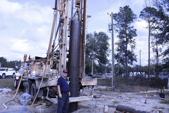 Fire Chief Dennis Russell stands next to the rig that is drilling a fire suppression well for the firehouse.