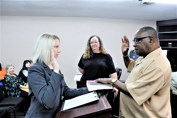 Judicial Assistant Mandy Waters swears in Franklin Schuler as a councilman while fellow council member, already sworn, Virginia Phillips looks from the background.