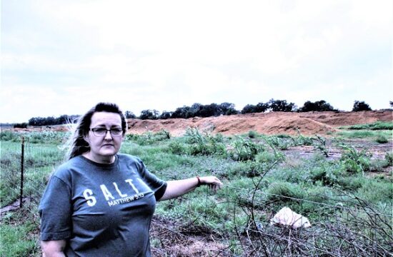 Rose Fant stands along her fence line with the manure composting facility, or manure muck dump facility, in the back of her.