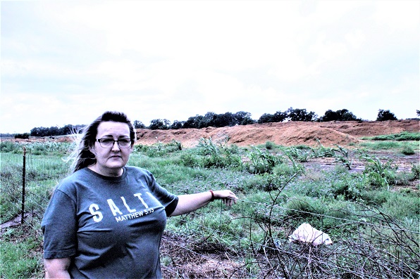 Rose Fant stands along her fence line with the manure composting facility, or manure muck dump facility, in the back of her.