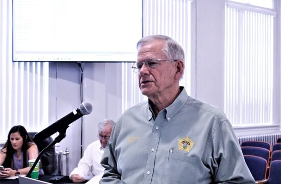 Sheriff Bobby McCallum got more than he bargained for at Tuesday's Levy County Commission budget hearing. He walked away smiling. Pictured behind him on the left are Procurement Coordinator Alicia Tretheway and County Coordinator Wilbur Dean.